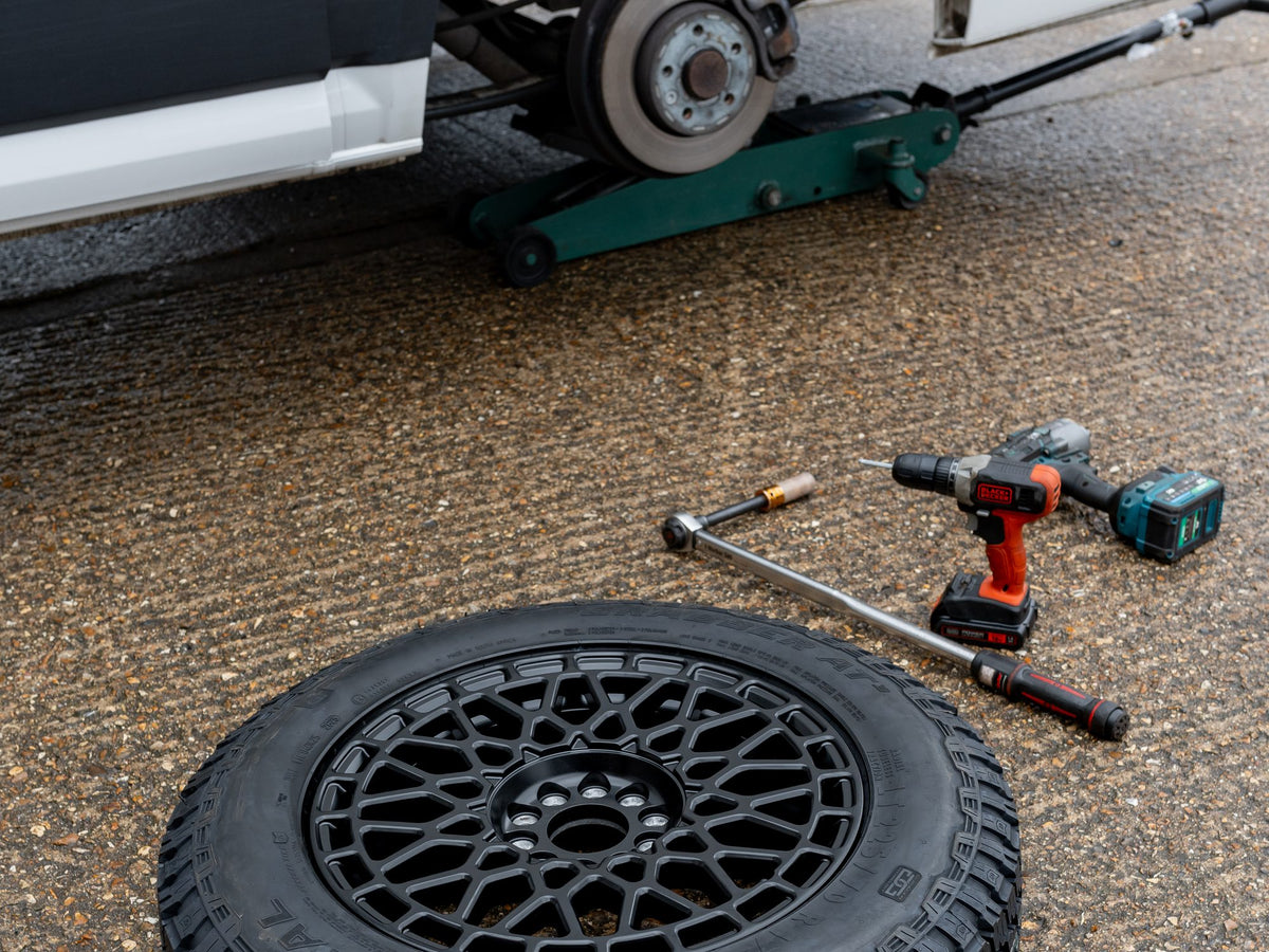 A van's hub and studs exposed on the jack, a torque wrench beside the new Rogue wheel and tyre