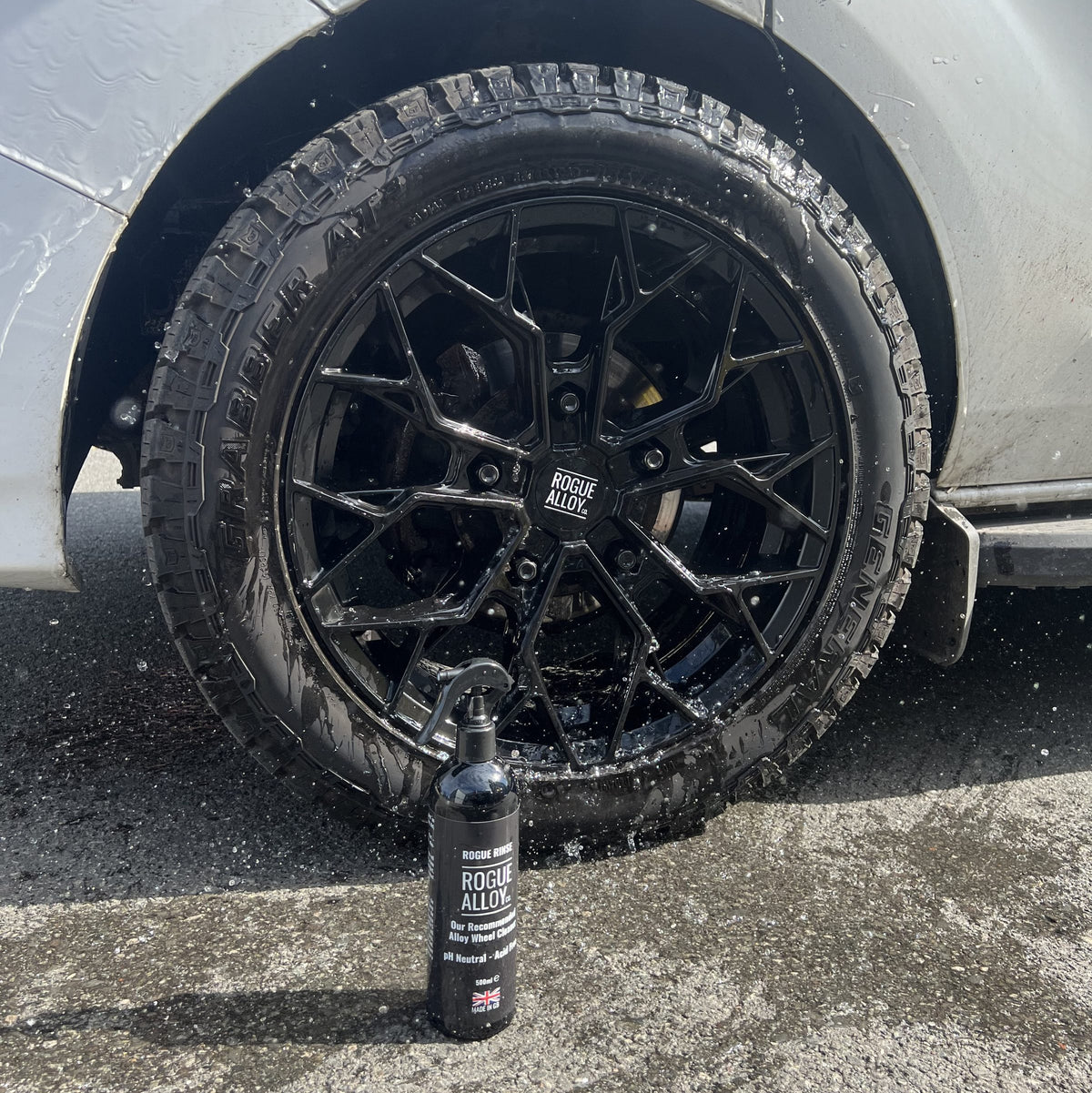 A just-rinsed black Rogue wheel with a bottle of Rogue Alloy Rinse on the wet tarmac