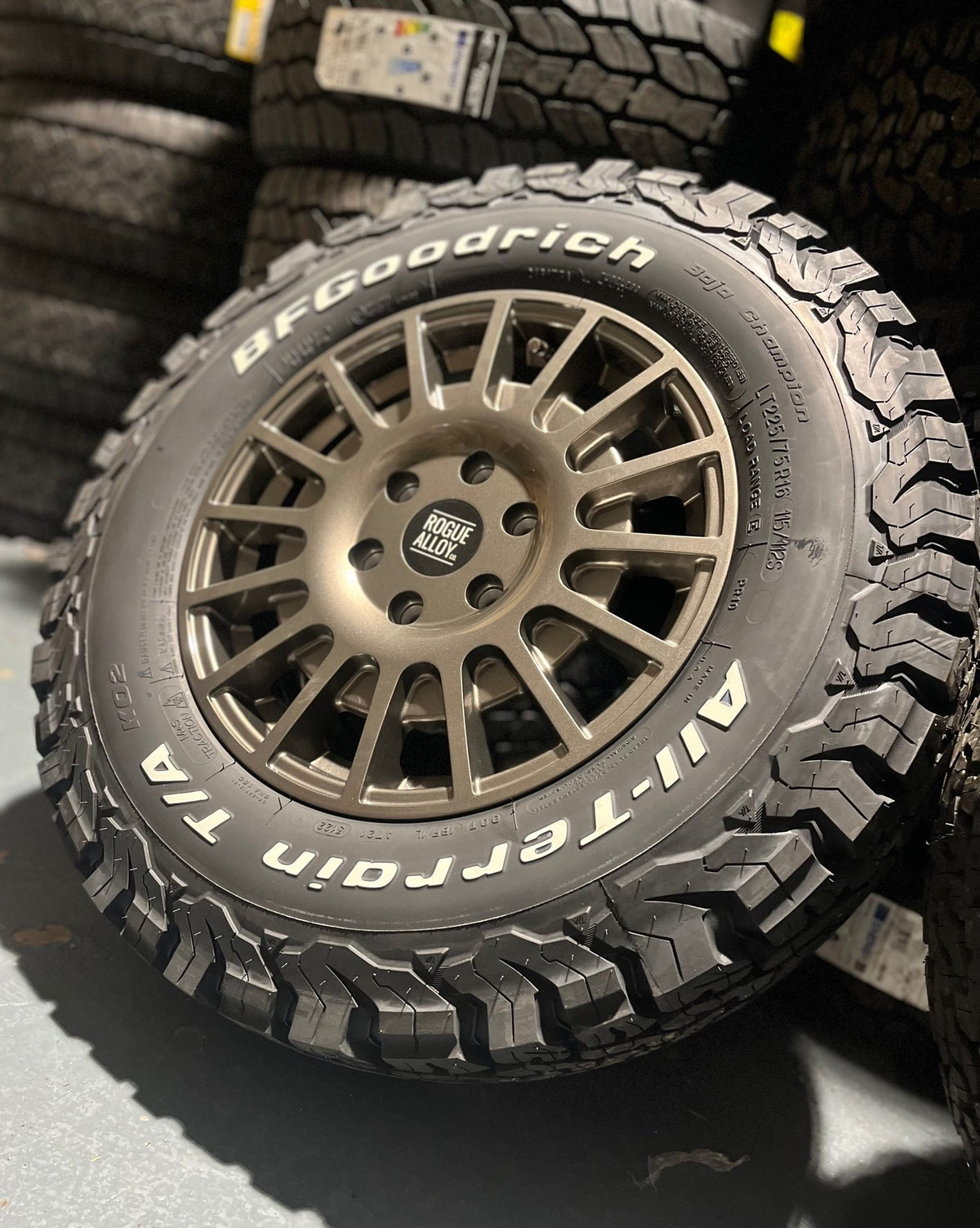 A BFGoodrich All-Terrain tyre on a bronze Rogue wheel in front of our tyre racks